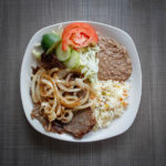 steak and onions with rice, beans, and salad on white plate