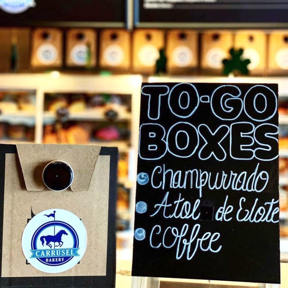 To go box with carrusel bakery logo next to a sign that says to go boxes, champurrado, atol de elote, coffee